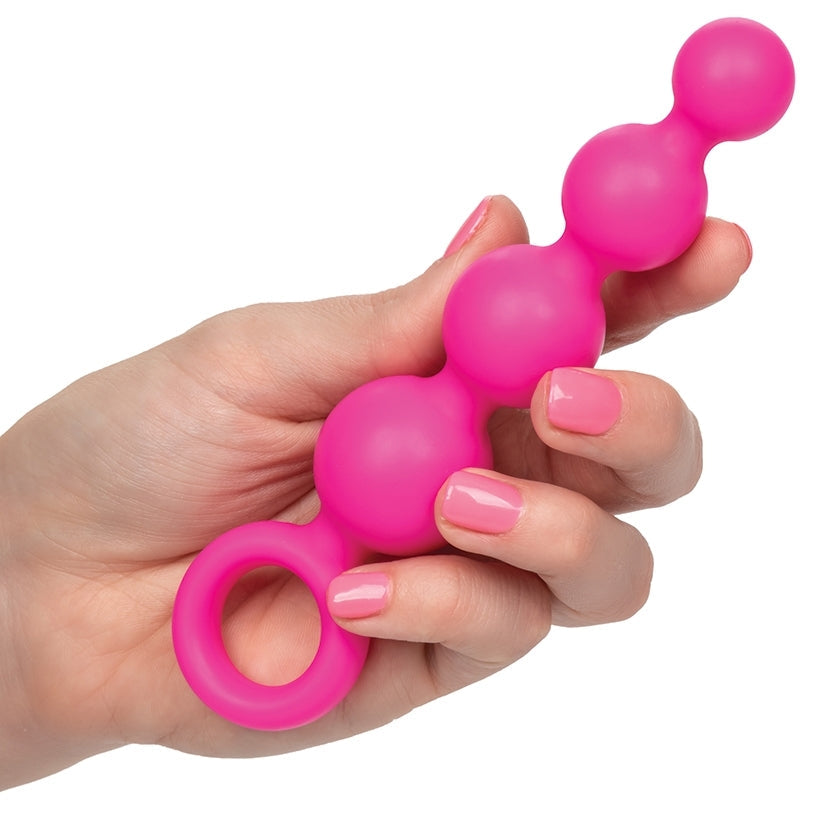 Hand holding a pink silicone tool with multiple nodes on a white background